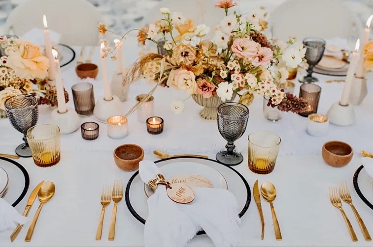 An Estancia 5-course wedding tablescape — ivory linen, dusty pink and amber florals, smoky glass goblets, gold cutlery.